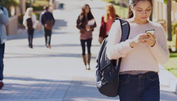 female student walking on campus looking at her phone