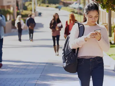 female student walking on campus looking at her phone