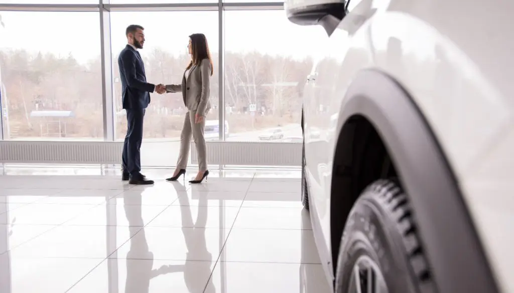 man and woman in a car dealership shaking hands