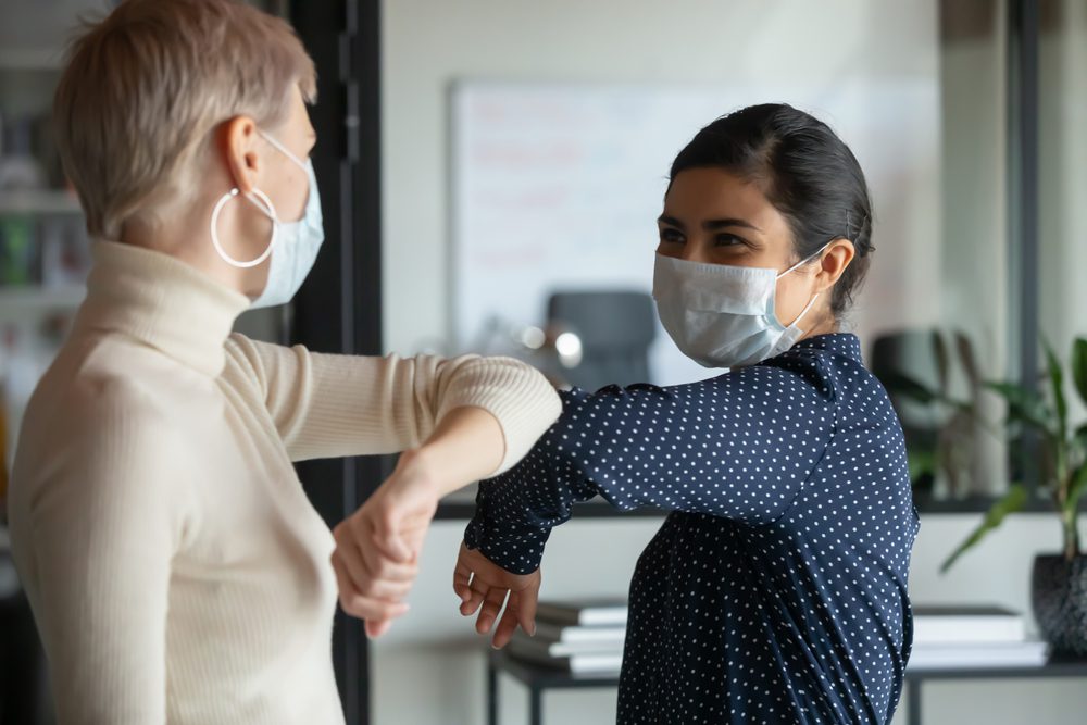 Smiling diverse Female Colleagues Wearing Protective Face Masks Greeting