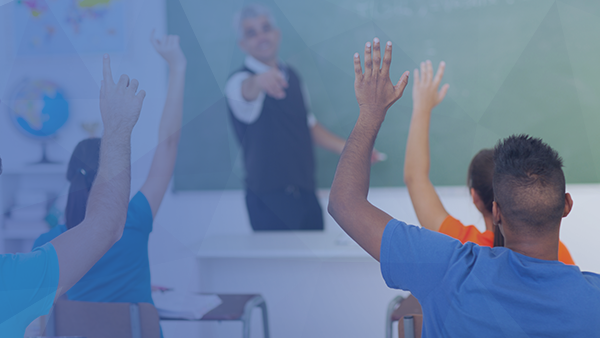 students in classroom with teacher standing at front of class as kids raise hands