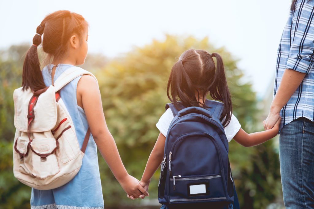 children holding hands with backpacks on