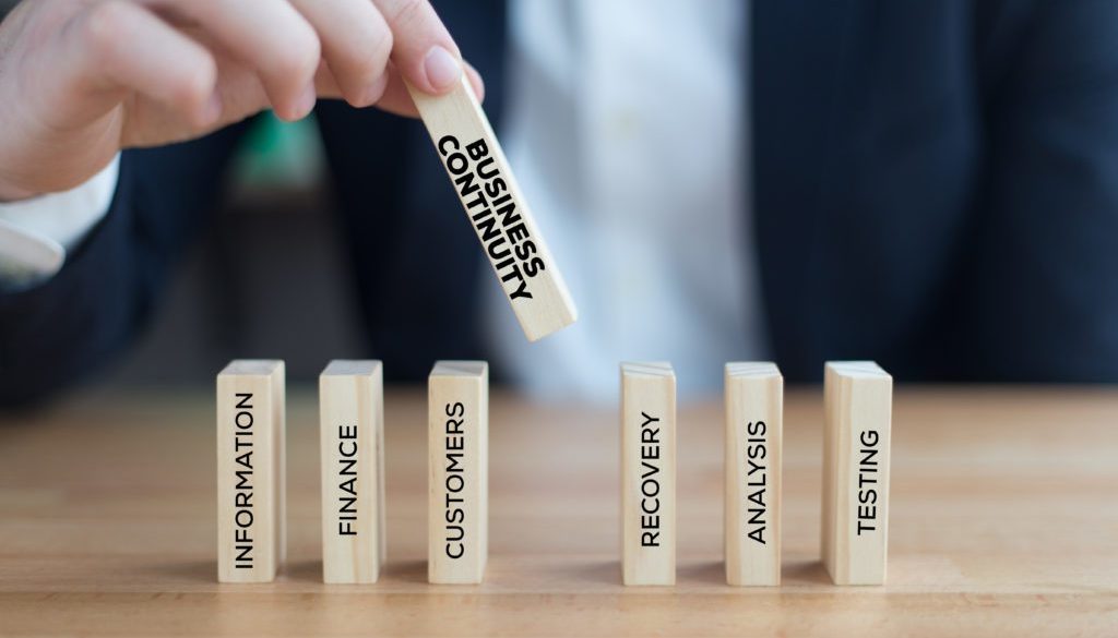 hand placing a domino titled "business continuity" onto a table