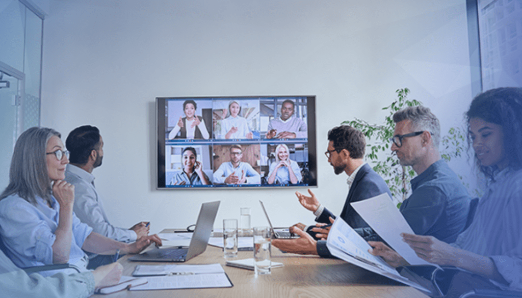 employees working at a conference table with remote employees on tv screen